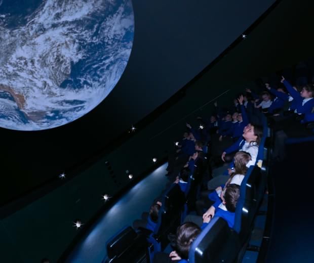 A group of schoolchildren watch a film on a planetarium screen