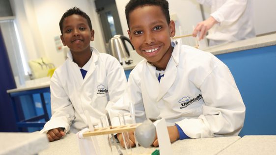 Two children wearing lab coats with test tubes in front of them as part of a schools session.