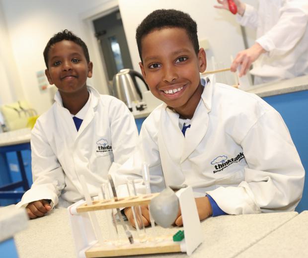 Two children wearing lab coats with test tubes in front of them as part of a schools session.