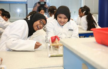 Two girls laughing girls wearing lab coats performing an experiment with test tubes.
