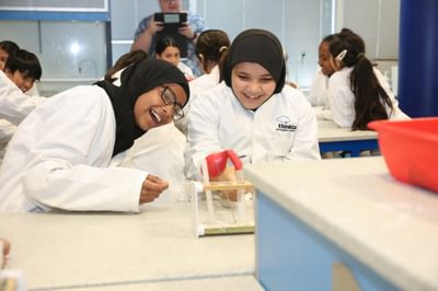 Two girls laughing girls wearing lab coats performing an experiment with test tubes.