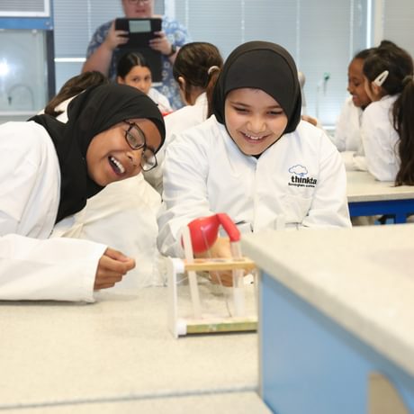 Two girls laughing girls wearing lab coats performing an experiment with test tubes.