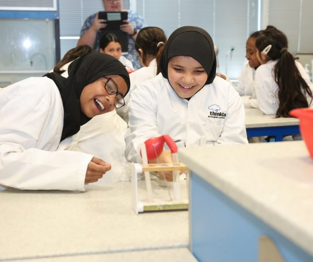 Two girls laughing girls wearing lab coats performing an experiment with test tubes.