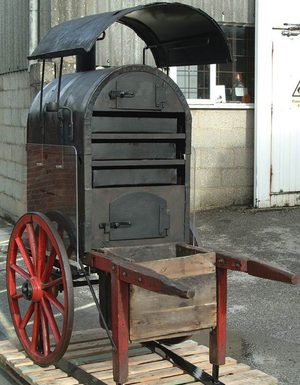 Metal oven on two wheels with two wooden legs and handle to one end