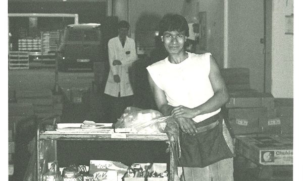Black and white photo a of a man standing next to a refreshment trolley in a market.