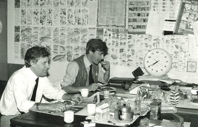 A black and white photo of two men sitting at a table eating breakfast.
