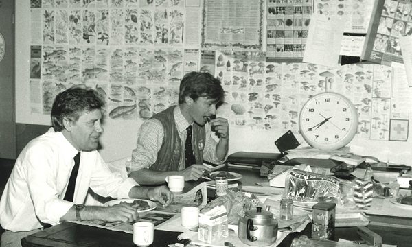 A black and white photo of two men sitting at a table eating breakfast.