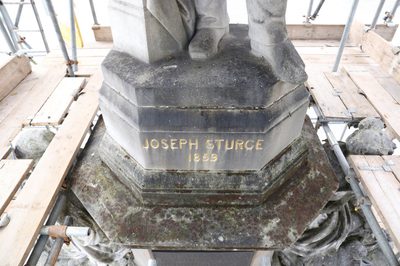 Base of the statue with dirt and moss with 'Jospeh Sturge 1859' in gold lettering.