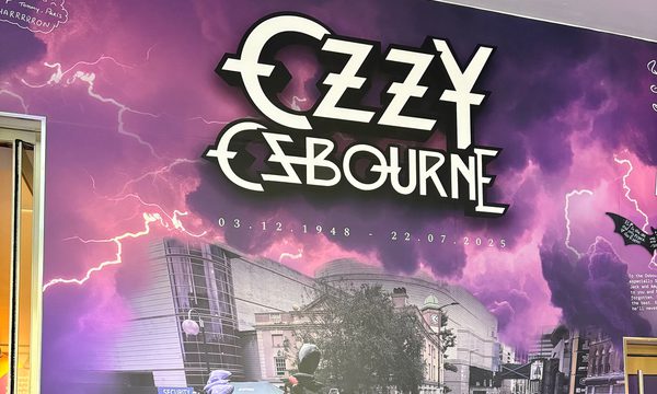 Tribute wall which reads "Ozzy Osbourne 3.12.1948 - 22.7.2025 Forever the pride of Brum. Along side a photo of a crowd of people leaving tributes on near the Black Sabbath bench.