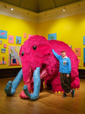 Joe Lycett standing next to a large pink woolly mammoth artwork.