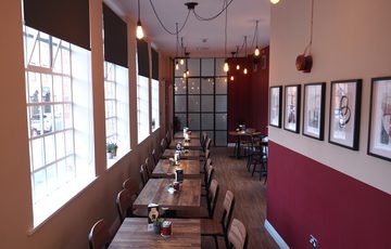 Interior of a cafe bar with large windows, tables lined up in a row with burgundy and cream walls.