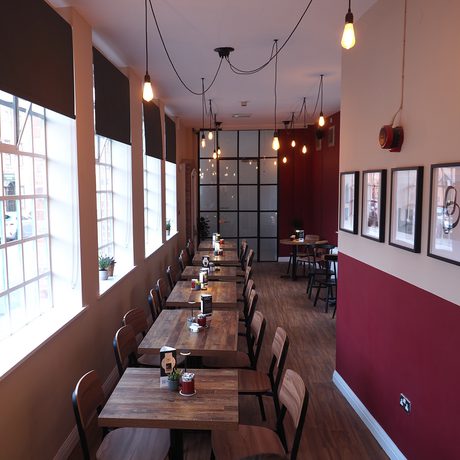 Interior of a cafe bar with large windows, tables lined up in a row with burgundy and cream walls.