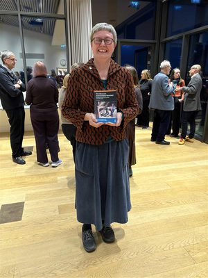 A person smiling and standing holding a book.