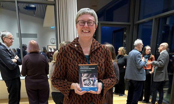 A person smiling and standing holding a book.