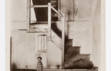 An old sepia photograph of a small twisted staircase leading to a doorway and room beyond.