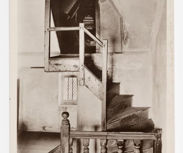 An old sepia photograph of a small twisted staircase leading to a doorway and room beyond.