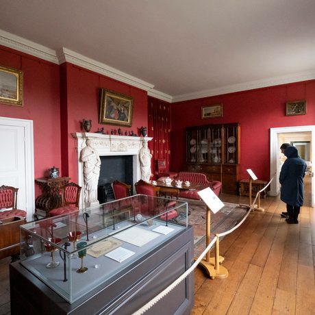 Visitors in the room painted red with furniture and and fireplace.