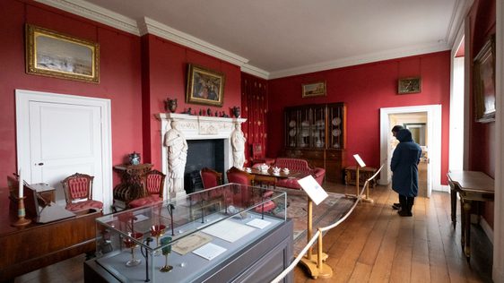 Visitors in the room painted red with furniture and and fireplace.