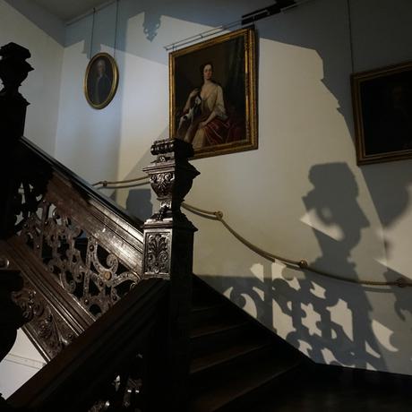 The stairs at Aston Hall at night. Shadows of the wooden staircase can be seen on the walls.