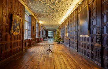 Jacobean wood-panelled Long Gallery with leaded windows, ornate fireplace and plaster ceiling. Decorated with two large Christmas trees.