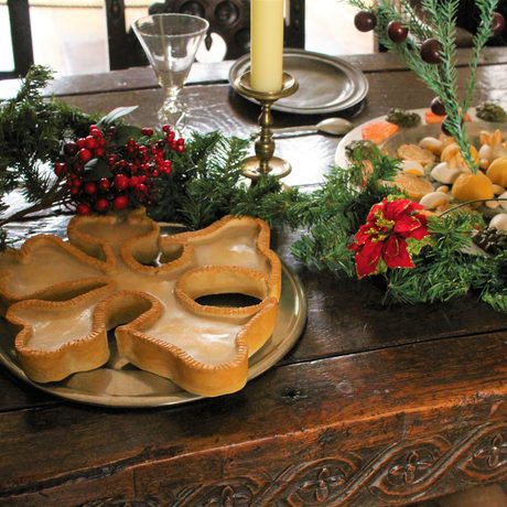 Close up of food on a table decorated with Christmas garland berries. A tree is behind.