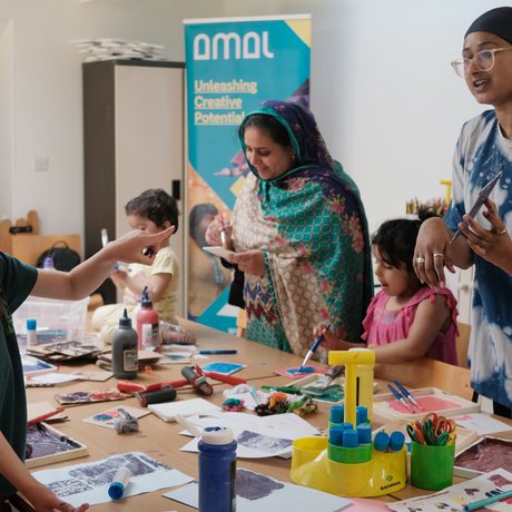 A group of adults and children are around a table which has lots of art supplies on it.