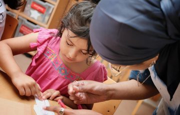 An adult helping a child with an art activity at a table.