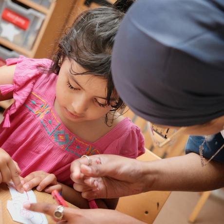 An adult helping a child with an art activity at a table.