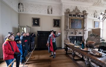 A tour guide dressed as Sir Thomas Holte giving a tour to a group of adults and children. They are in a in Great Dining Room.