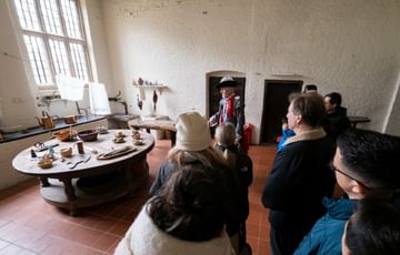 A tour guide dressed as Sir Thomas Holte giving a tour to a group of adults and children. They are a in an old kitchen.