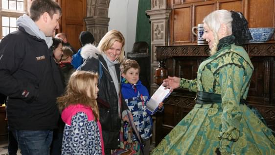 A family of two adults and two children meeting a female reenactor wearing an historical style dress