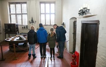 A family in a Jacobean kitchen with tiled floors and tall windows.