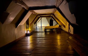 An attic bedroom with slanted ceilings, wooden floors, candle lighting, and a single bed.