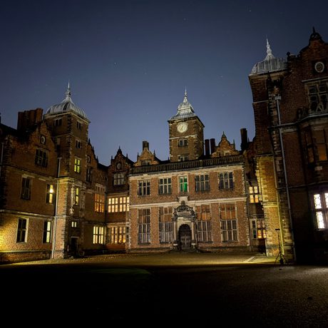 Illuminated historic mansion with intricate architecture against a dark night sky.
