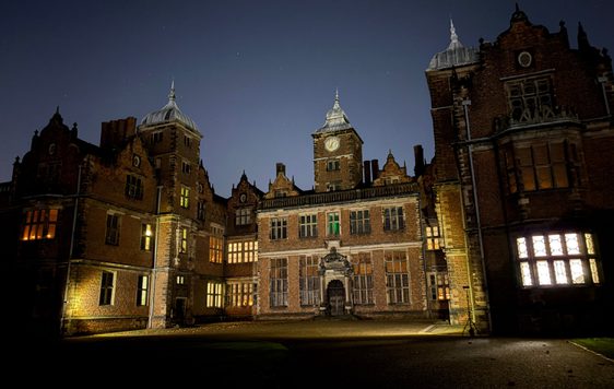 Illuminated historic mansion with intricate architecture against a dark night sky.