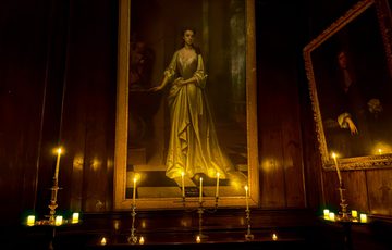 Dimly lit room with portraits, candles, and warm wooden paneling.
