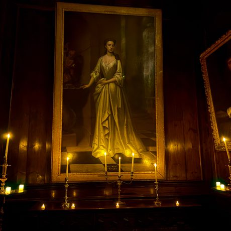 Dimly lit room with portraits, candles, and wooden paneling.
