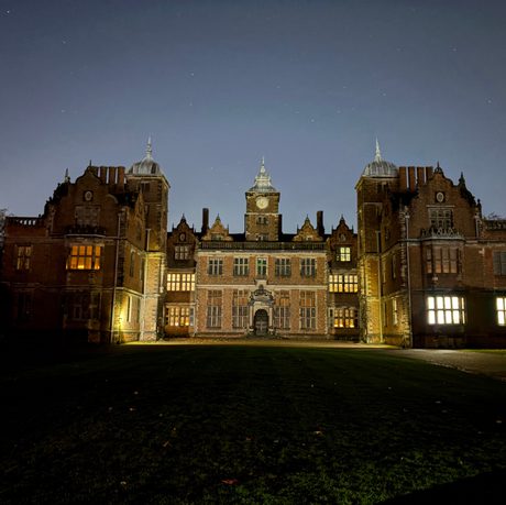 Exterior of Aston Hall at night, with windows glowing by candlelight.