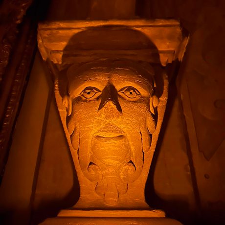 Ornate carved face in the wall lit with a candle.