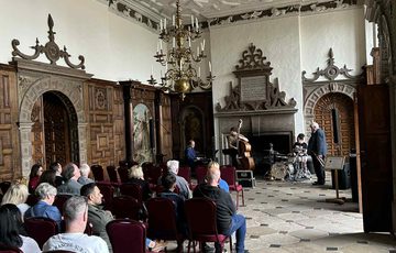 People sitting listening to a Jazz band in a historic grand hall.