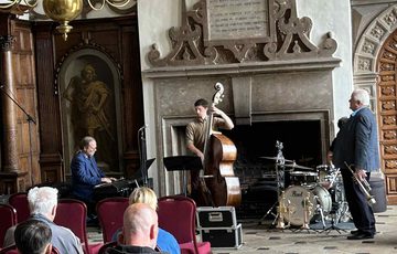 People sitting listening to a Jazz band in a historic grand hall.