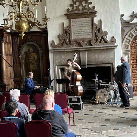 People sitting listening to a Jazz band in a historic grand hall.
