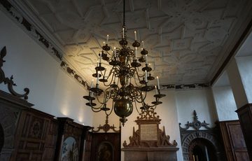 A large chandelier hanging from an orate ceiling in a great Hall.
