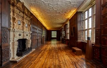Jacobean wood-panelled Long Gallery with leaded windows, ornate fireplace and plaster ceiling.