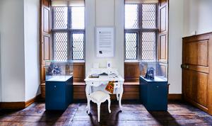 A room with two tall windows with a display case in front of each window and a dressing table in the middle.