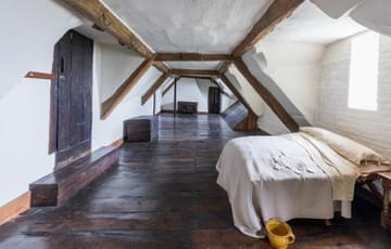 A basic bedroom in the eaves with wooden floor and doors and bed.