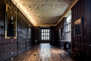 Wood-panelled Jacobean long gallery with ornate plaster ceiling, oil paintings are hanging on the walls