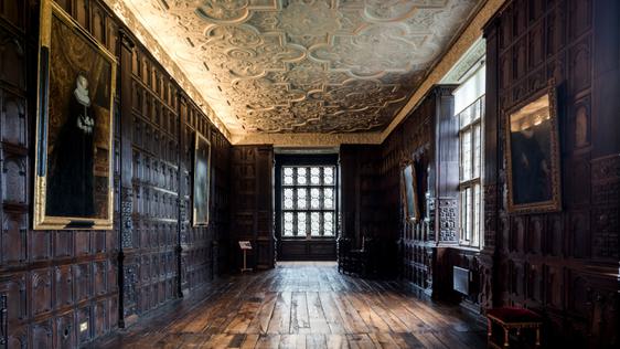 Wood-panelled Jacobean long gallery with ornate plaster ceiling, oil paintings are hanging on the walls