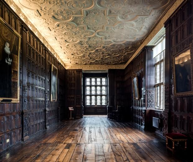 Wood-panelled Jacobean long gallery with ornate plaster ceiling, oil paintings are hanging on the walls