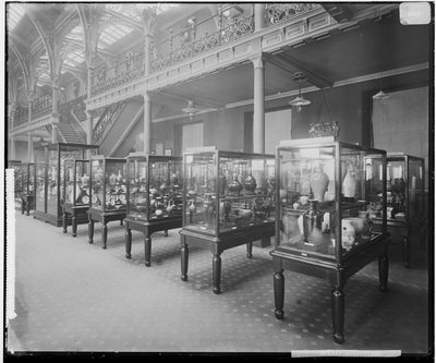 Black and white photo of part of the Industrial Gallery with rows of glasses cases containing objects.